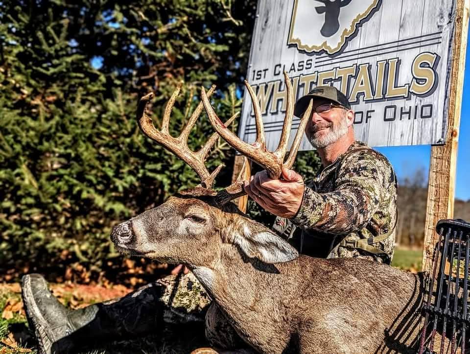 Hunter with a mature Ohio whitetail buck in front of the 1st Class Whitetails sign