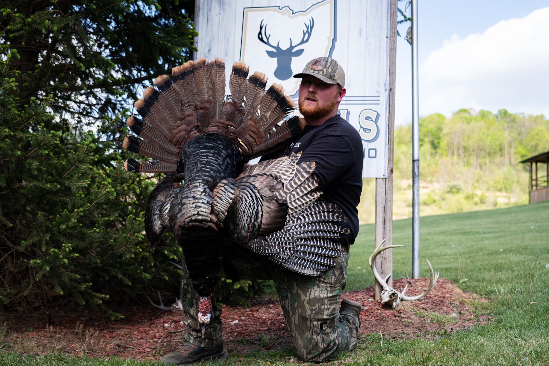 Hunter with a longbeard tom in front of the 1st Class Whitetails of Ohio sign