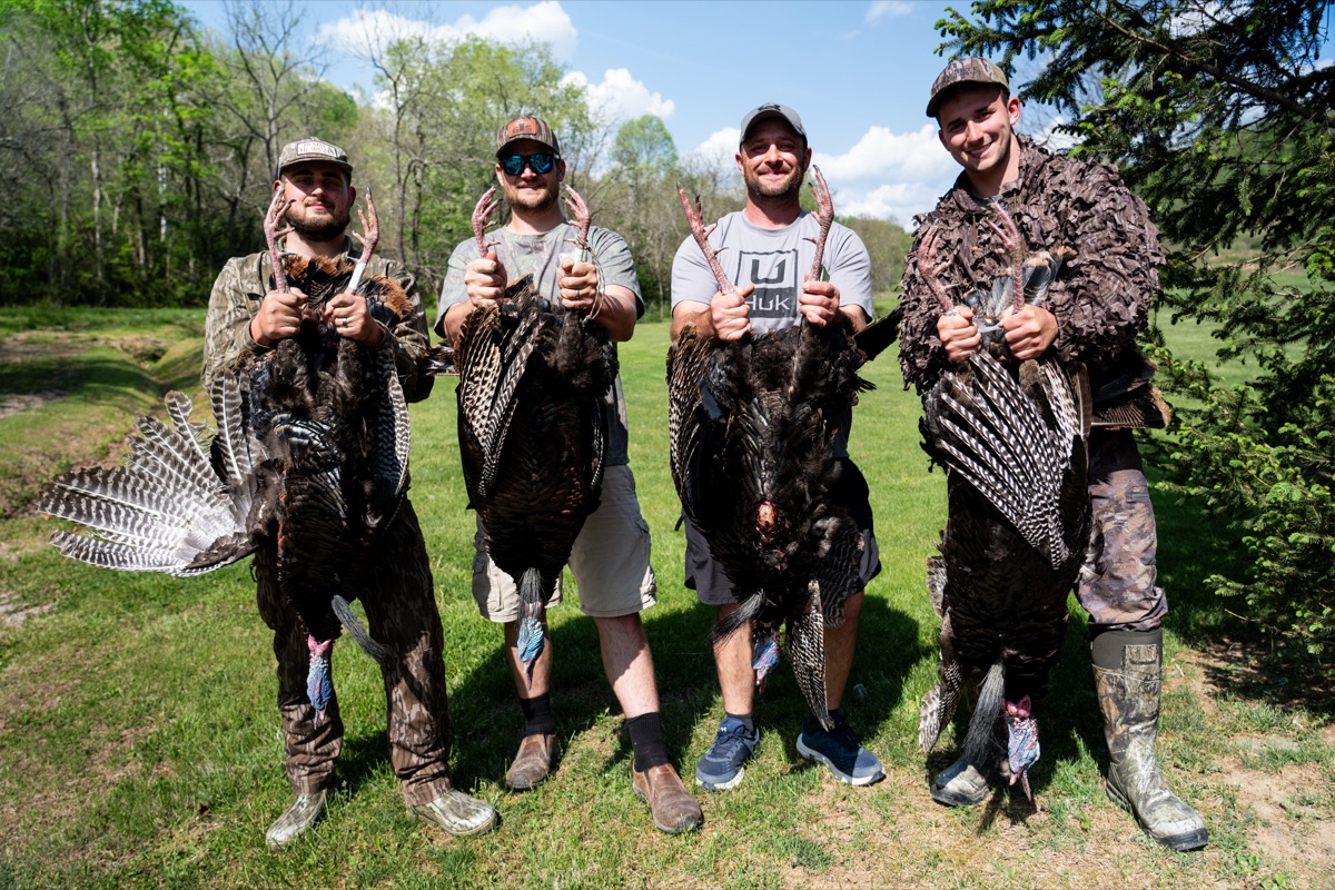Four hunters holding their toms by the feet to display spurs for NWTF scoring